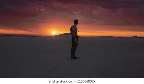 Man looking at desert sunset while exercising. Male athlete taking break from exercising on sand dunes.