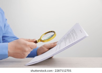 Man looking at document through magnifier at white wooden table, closeup. Searching concept