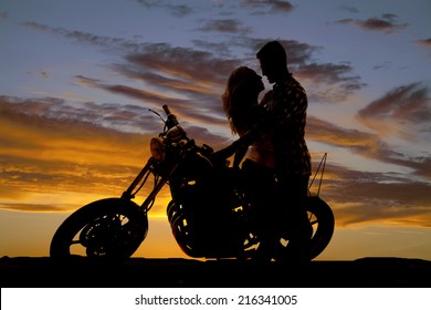 A man looking down at his woman, as she sits on a motorbike, looking into her eyes.