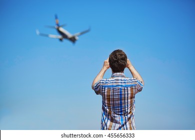 Man is looking at the glide path and landing plane or taking a photo of it. Aircraft spotting concept