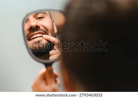 Man looking at himself in a mirror, checking his teeth and smile. Concept of dental care, oral hygiene, and routine checkup