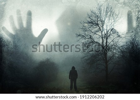 A man looking up at a huge ghostly hooded figure appearing out the mist. On a moody winters day in the countryside. With a grunge, vintage edit.