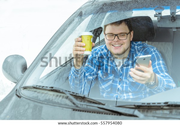 man looking info in phone and drinkig coffie while\
sitting in car