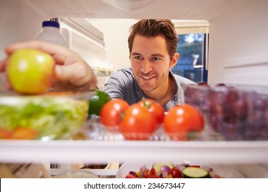 Man Looking Inside Fridge Full Of Food And Choosing Apple