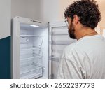 Man looking into empty refrigerator in modern kitchen