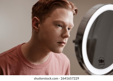 Man Looking into Vanity Mirror Preparing for Skincare Routine
A young man looks thoughtfully into a vanity mirror with LED lighting, preparing for a skincare or grooming routine. 
sstkDiverseBeauty