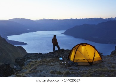 Man looking at lake by illuminated tent at dusk - Powered by Shutterstock