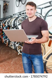 Man Is Looking In Laptop And Choosing Modern Bicycle In The Bike Store.