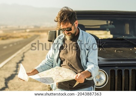 Man looking at map leaning on vehicle at roadside. Mature man checking location of destination on paper map standing outside car. Man searching for navigational route using paper map at roadside
