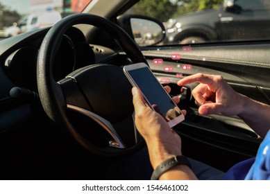 Man looking at mobile phone while driving a car.Dangerous driver ,or Young male driver using touch screen smartphone and gps navigation in a car.