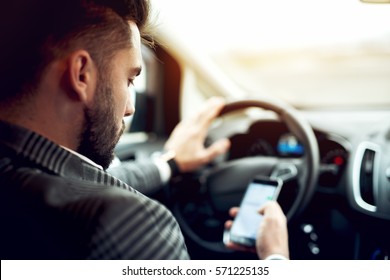 Man looking at mobile phone while driving a car. - Shutterstock ID 571225135