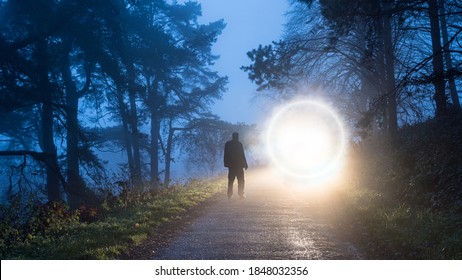 A Man Looking At A Mysterious Glowing Portal  On A Forest Road On A Foggy Winter Evening.