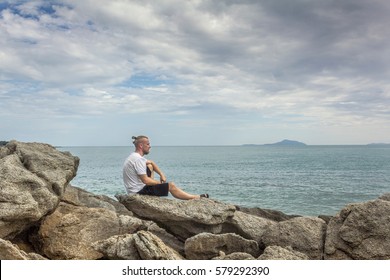 Man looking at the ocean. Horizontal side view of a person looking at the ocean sitting on a stone. 