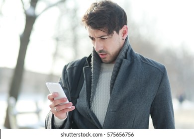 Man Looking On His Smartphone Unhappily With Disbelief At The Winter Snowy Park