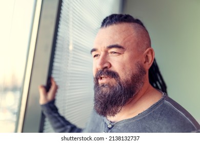 Man looking out the window. Portrait of an adult man with a mohawk and dreadlocks. A middle-aged man with a beard and an unusual hairstyle.