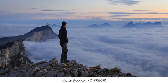 A man looking over a sea of clouds in the mountains at dawn.