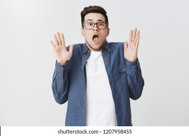 Man Looking Pale And Scared As Seing Ghost Gasping Dropping Jaw Tilting Backwards And Raising Hands In Surrender Being Terrified By Scary Prank Of Friends Standing In Stupor Over Gray Background