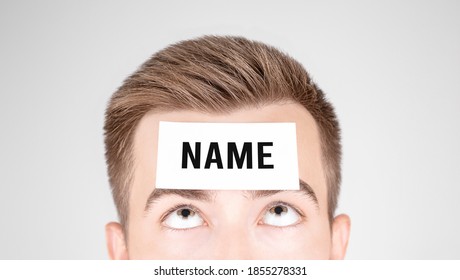 Man Looking At Paper With Word Name Pasted On His Forehead