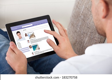 Man looking at personal profiles or comments left by viewers on a tablet computer navigating the touch screen with his finger  over the shoulder view of the screen - Powered by Shutterstock