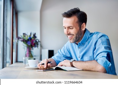 Man Looking At Phone And Writing In Calendar While Out For Coffee In Cafe