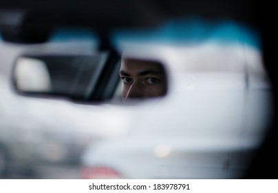 Man Looking In The Rear View Mirror While Driving The Car, Focus To The Mirror With Just His Eyes Visible