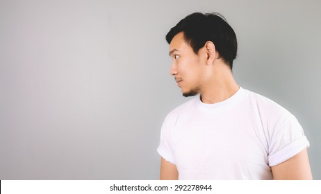 A man looking at the side of empty copyspace. An asian man with white t-shirt and grey background.