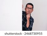 A man looking something from behind white wall with confused expression