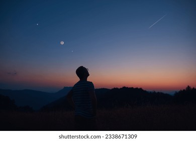 Man looking at the starry skies, crescent Moon and shooting star in blue hour twilight time. - Powered by Shutterstock