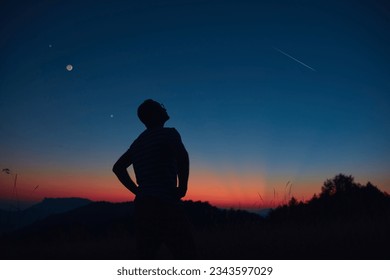 Man looking at the starry skies, crescent Moon and shooting star in blue hour twilight time. - Shutterstock ID 2343597029