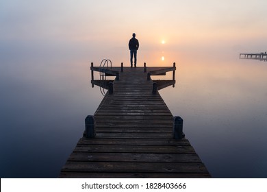 A man looking at the sunrise on a  foggy, tranquil morning.