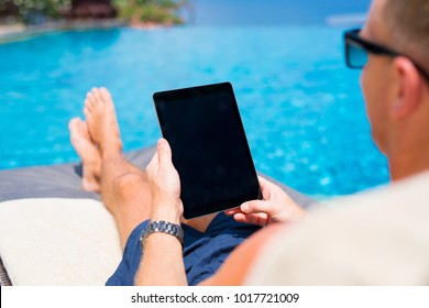 Man looking at tablet computer while sunbathing by the pool.