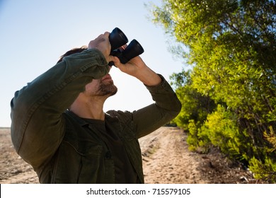 Man looking through binocular while standing by trees on field