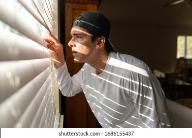 A man looking through the blinds of a window as he is locked down on quarantine. - Powered by Shutterstock