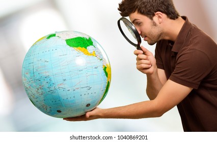Man Looking Through Magnifying Glass At Globe, Indoors