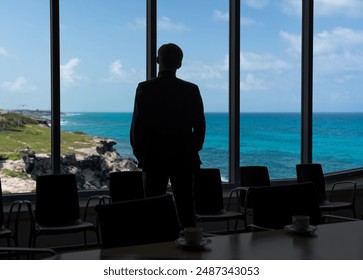 Man looking through office window dreaming about ocean beach. Vacation concept