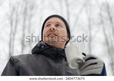 Man looking up while breathing cold air on a snowy winter day outdoors. Guy in a black beanie with mouth open in freezing weather. Adventurous spirit of a winter hike through a frosty landscape