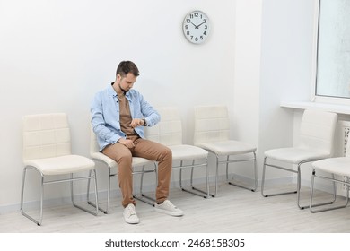 Man looking at wrist watch and waiting for appointment indoors