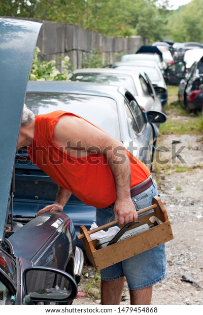 A man looks for car\
parts under the hook of a decommissioned junk car at an automotive\
recycking yard.