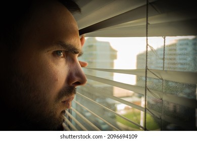 A Man Looks At The City Through The Dirty Window Through The Blinds With A Disgruntled Look. Close-up