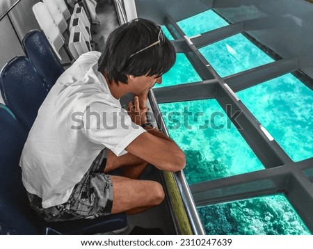 A man looks at the deep underwater life of the Red Sea through the transparent bottom of the bathyscaphe. Tourist marine service in Sharm El Sheikh, Egypt