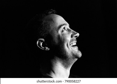 A Man Looks Happy And Laughing In The Moonlight. Low Key Black And White Profile Photo On Black Background
