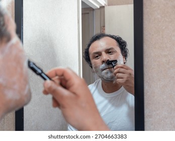 A man looks at himself in the mirror while shaving.