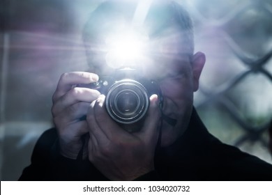a man looks into the camera's viewfinder and takes pictures using a flash, a photographer on the background of a metal grating, a selfie in a gloomy room - Shutterstock ID 1034020732