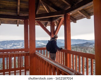Man looks into the distance on top of wooden observation tower. Eliaszowka Mountain in Beskid Sadecki in winter, Poland.