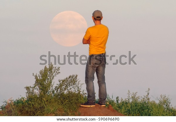 Man\
looks at a large full moon rising over the\
horizon