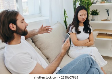 A man looks at the phone screen during an argument with his girlfriend. The angry and hurt woman looks in his direction and is sad. Family discord at home, phone addiction - Shutterstock ID 2230607965