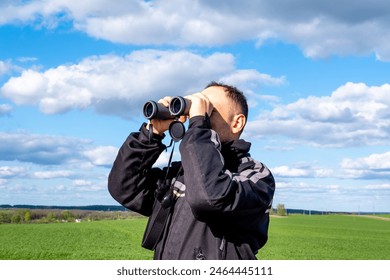 a man looks through binoculars on a road in a field - Powered by Shutterstock