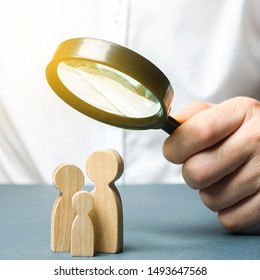 A man looks through a magnifying glass at a family figure. The study of family composition and demographic situation. Statistical data. The program of support for young families, financial assistance. - Powered by Shutterstock