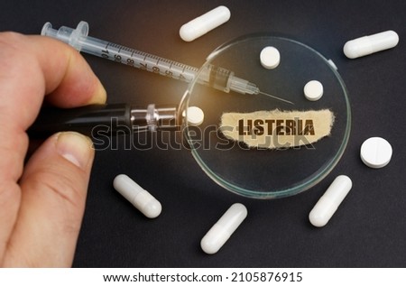 A man looks through a magnifying glass at pills, a syringe and a piece of paper with the inscription Listeria