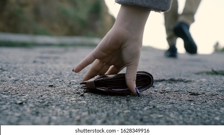 Man lost money purse on the street. Only his legs walking away in the picture, general focus on the wallet. Close-up Of A Woman Picking Up Fallen Wallet On road side. Selective focus